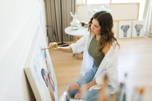 Talentosa joven artista femenina terminando una hermosa pintura con un pincel y sintiéndose creativa - Foto, Imagen
