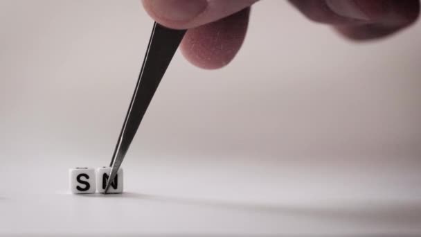 Der Satz Sneak Peek erscheint Buchstabe für Buchstabe auf weißem Hintergrund von einer Hand mit einer Pinzette - Filmmaterial, Video