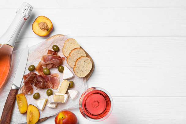 Delicious rose wine and snacks on white wooden table, flat lay. Space for text - Foto, imagen