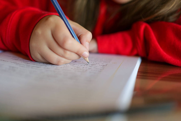 Homework.girl tekee kotitehtävänsä.lyijykynä lapsen kädessä kirjoittaa sanoja muistikirjaan.Opiskelu ja koulutus käsite. lapsi kirjoittaa kynällä muistikirjaan.  - Valokuva, kuva