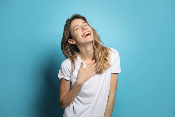 Cheerful young woman laughing on light blue background - Photo, Image