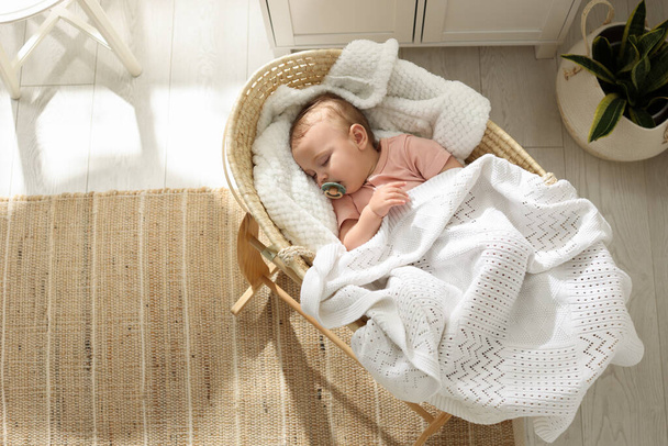 Cute little baby with pacifier sleeping in wicker crib at home, top view. Space for text - Foto, Imagen