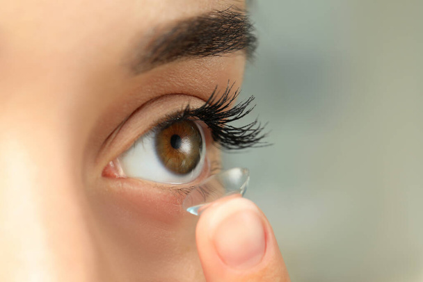 Woman putting contact lens in her eye on blurred background, closeup - Foto, Imagem