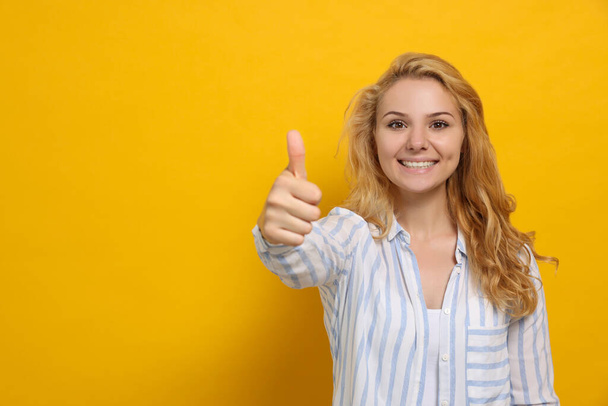 Happy young woman showing thumb up gesture on yellow background. Space for text - Foto, imagen