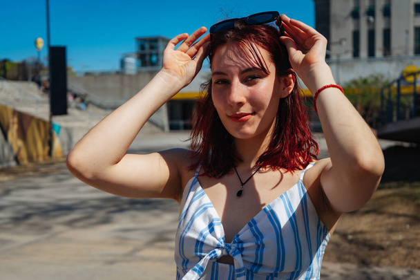 A Portrait of attractive redheaded young woman adjusting her sunglasses on her head. Copy space. Horizontal orientation. - 写真・画像