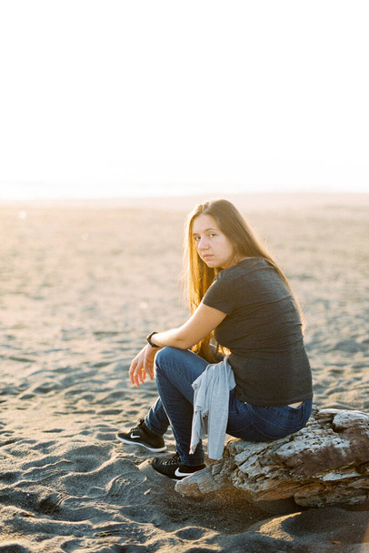 Chica en jeans se sienta en un enganche en una playa de arena. Foto de alta calidad - Foto, imagen