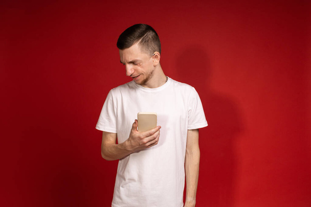 Un joven con una camiseta blanca con síndrome de Treacher sostiene un teléfono, personas con discapacidades, enfermedades genéticas - Foto, imagen