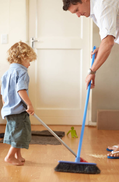 Cleaning cutie. A father and toddler son sweeping up sand together in their home - Foto, Bild