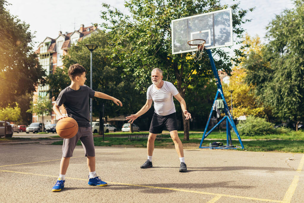 スポーツグラウンドでバスケットボールの試合を楽しむ父と息子 - 写真・画像