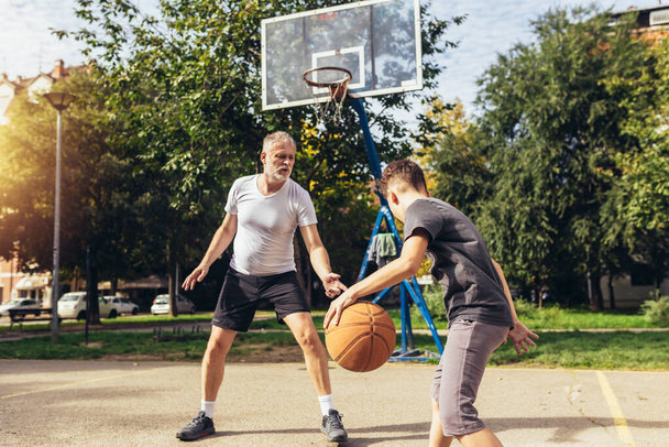 スポーツグラウンドでバスケットボールの試合を楽しむ父と息子 - 写真・画像