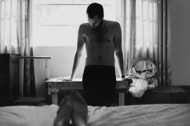 Küzd a bűntudat és a megbánás súlya alatt. Egy fiatal férfi áll az ágy végében, és lenéz szégyenében szex után. - Fotó, kép