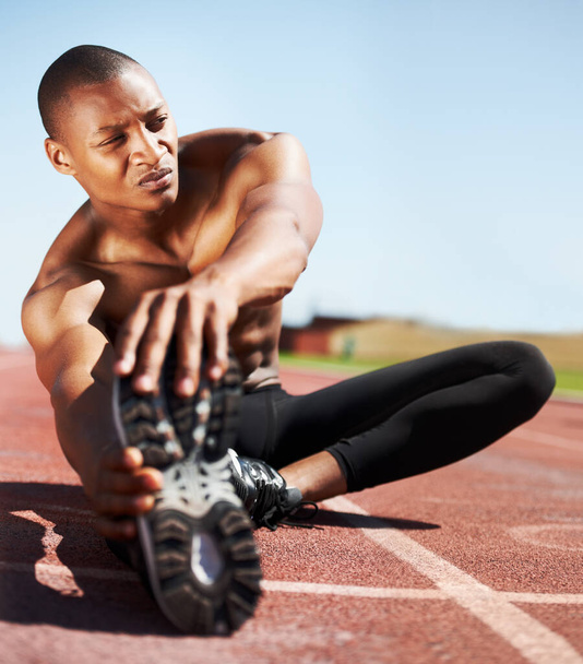 Preparing to win. an athlete stretching his legs while sitting on the track - 写真・画像