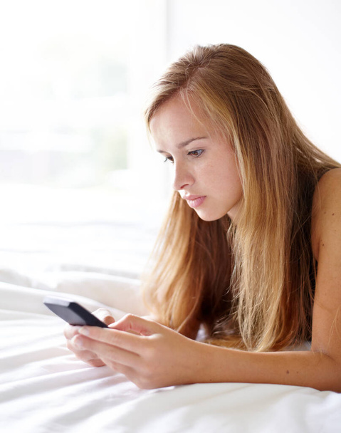 Beírom a tökéletes választ. egy gyönyörű fiatal nő, aki SMS-t olvas miközben fekszik az ágyán. - Fotó, kép