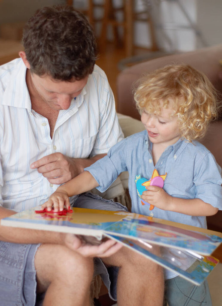 Un niño con talento en el juego. Un niño sonriente sosteniendo y ajustando piezas del rompecabezas mientras su padre sostiene un libro de rompecabezas - Foto, Imagen