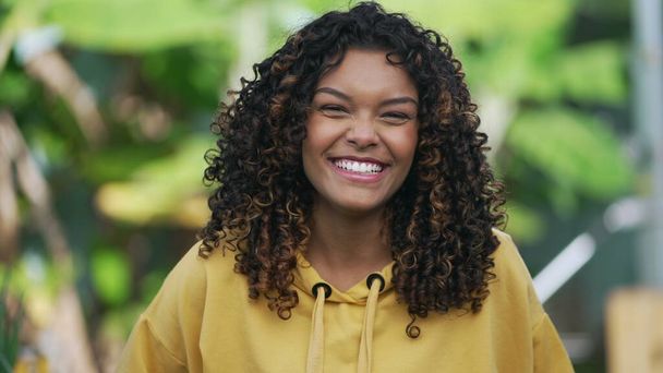 Portrait of a happy Brazilian black girl with curly hair. Young African American millennial 20s woman wearing yellow blouse looking at camera - Photo, Image