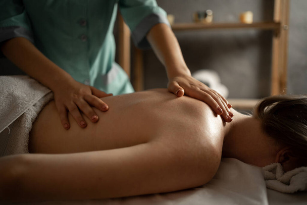 Masajista profesional haciendo masaje terapéutico. Mujer disfrutando de masajes en el salón de spa. Mujer joven recibiendo masaje corporal relajante. Concepto de cuidado corporal - Foto, Imagen