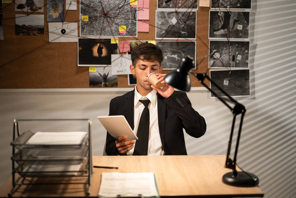 Detective working at desk in his office, drinking coffee and thinking of searching for solution, copy space - Foto, imagen