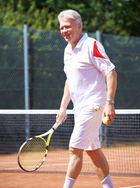 テニスは昔から彼のお気に入りだった。テニスの試合中に粘土のコートを歩く老人 - 写真・画像