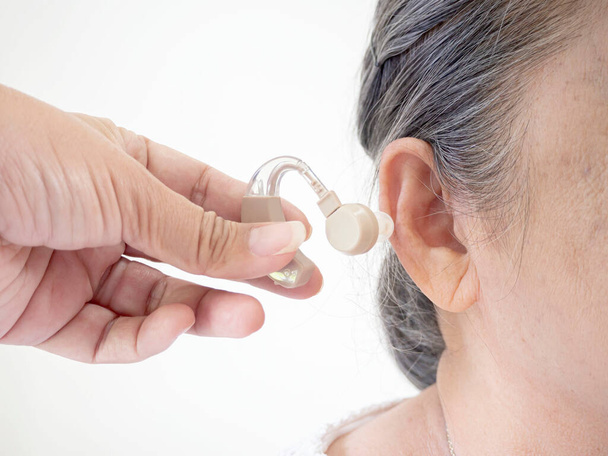 Close-up of hand helping senior patient with hearing aid, white blackground. - Fotoğraf, Görsel