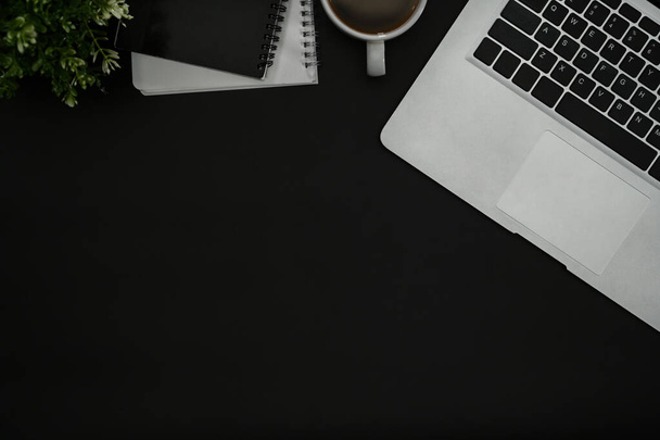 Schwarzer Schreibtisch mit Laptop, Kaffeetasse, Notizbuch und Topfpflanze. Draufsicht mit Kopierraum. - Foto, Bild