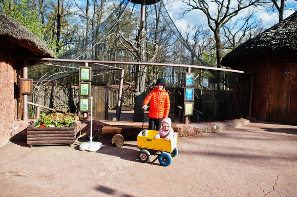 Boy pulls wooden trolley with sister at zoo. - Zdjęcie, obraz