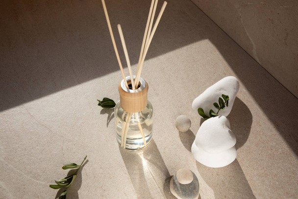 Aroma diffuser in a clear glass bottle with a wooden cap on a light stone background with wooden sticks behind and green branches. Top view - Photo, Image
