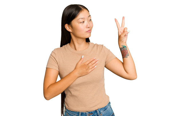 Fiatal ázsiai nő elszigetelt zöld króm háttér esküt, kezét a mellkason. - Fotó, kép