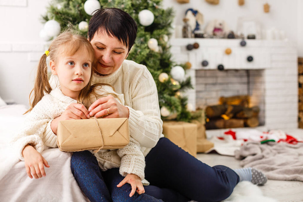 Mother and daughter unwrapping a present lying on the floor in the living room. - Foto, imagen