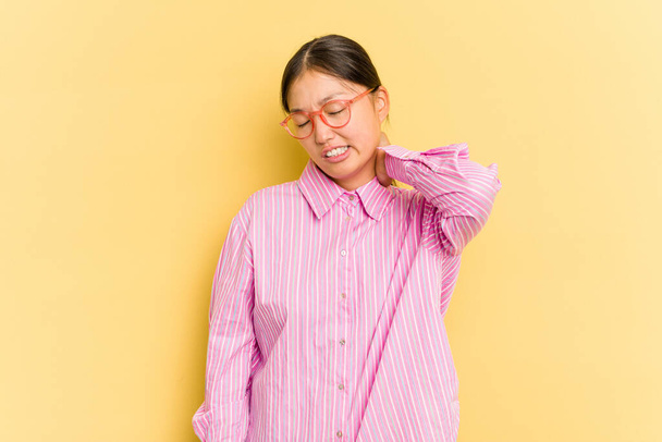 Mujer asiática joven aislada sobre fondo amarillo con dolor de cuello debido al estrés, masajeando y tocando con la mano. - Foto, imagen