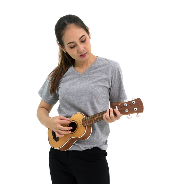 Aziatische vrouw in grijs t-shirt en zwarte broek op een Ukulele gitaar. Portret op witte achtergrond met studiolampje. - Foto, afbeelding