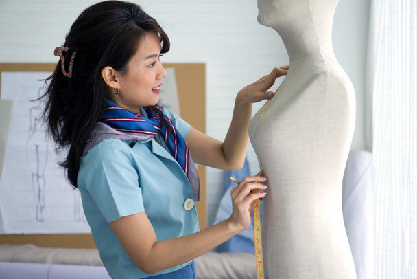 Chambre de créateur de mode. Jeune couturière asiatique en foulard rayé utiliser un ruban à mesurer, la taille de la poitrine de la mannequin. - Photo, image