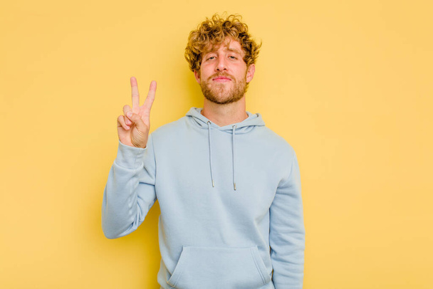Young caucasian man isolated on yellow background joyful and carefree showing a peace symbol with fingers. - Photo, Image