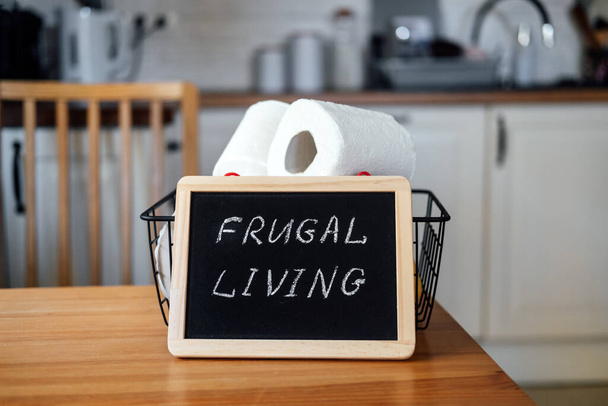Vivir frugal, ahorrar dinero, vivir concepto barato con cesta de papel higiénico y texto de vida frugal en el marco en la mesa de la cocina en casa. - Foto, Imagen