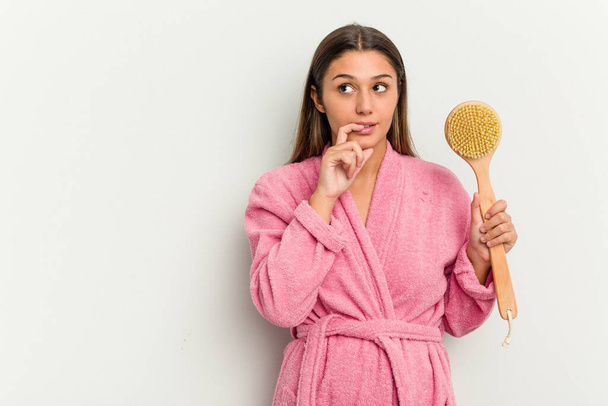 Young Indian woman holding a shower brush isolated on white background relaxed thinking about something looking at a copy space. - Foto, afbeelding
