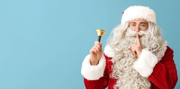 Weihnachtsmann mit Weihnachtsglocke mit Geste der Stille auf hellblauem Hintergrund mit Platz für Text - Foto, Bild