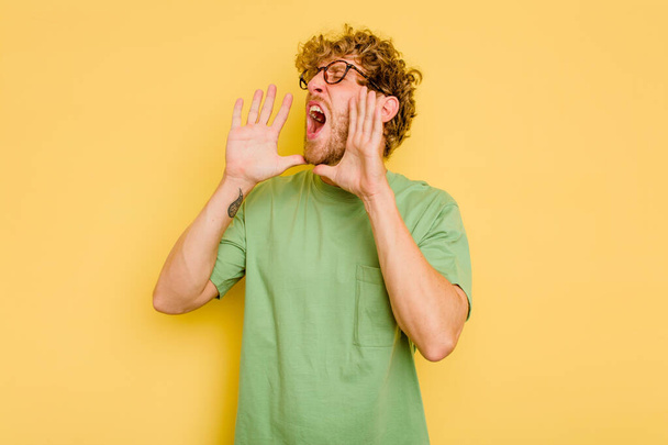 Young caucasian man isolated on yellow background shouting excited to front. - Foto, Imagen
