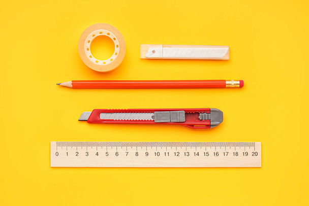 Utility knife with adhesive tape, blades, pencil and ruler on yellow background - Photo, Image