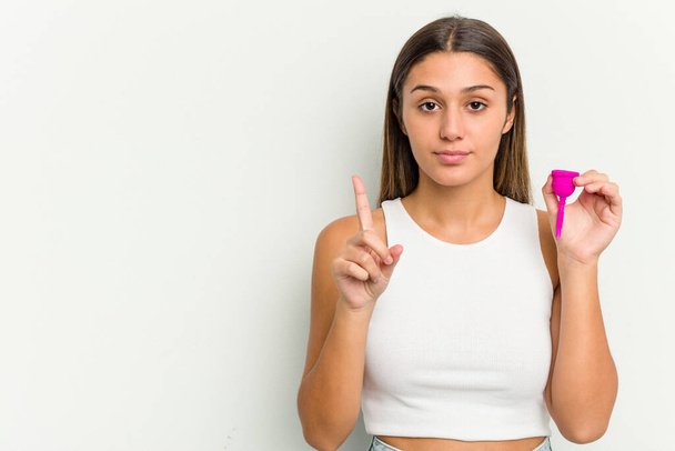 Mladá žena drží menstruační pohár izolované na bílém pozadí ukazující číslo jedna s prstem. - Fotografie, Obrázek
