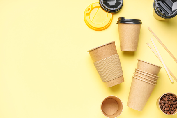 Χάρτινες κούπες, ξυλάκια και κόκκοι καφέ σε κίτρινο φόντο - Φωτογραφία, εικόνα