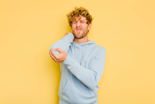Young caucasian man isolated on yellow background massaging elbow, suffering after a bad movement. - Photo, Image