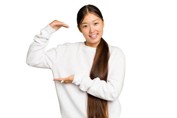 Young Asian woman isolated on green chroma background holding something little with forefingers, smiling and confident. - Photo, Image