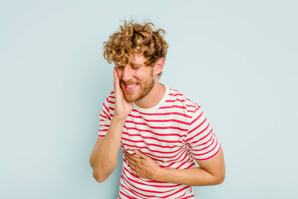 Young caucasian man isolated on blue background laughs happily and has fun keeping hands on stomach. - Foto, Bild