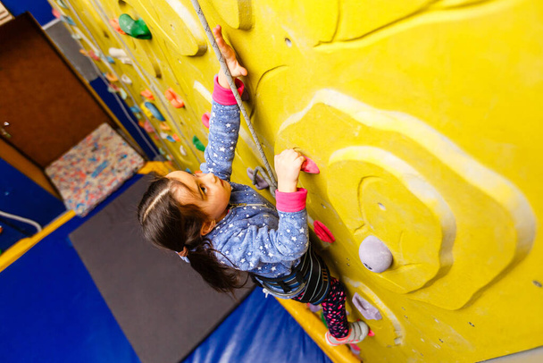 Little girl climbing a rock wall indoor - Foto, Imagen