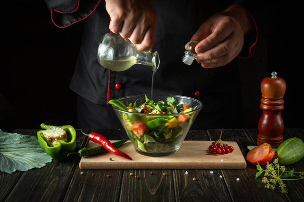 Ο σεφ προσθέτει αρωματικό λάδι στη σαλάτα λαχανικών. Χορτοφαγικά τρόφιμα από τα χέρια του μάγειρα στην κουζίνα. - Φωτογραφία, εικόνα