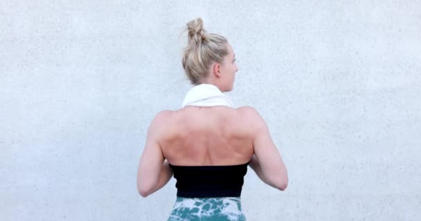 Half Body Taustakuva Shot of kuntosali Sopii valkoihoinen urheilullinen nainen pukeutunut urheiluvaatteet ja hänen hiukset ylös pitämällä pyyhe kaulassaan käsillään ja seisoo kuntosalilla. Taustalla seinään, takaisin - Materiaali, video