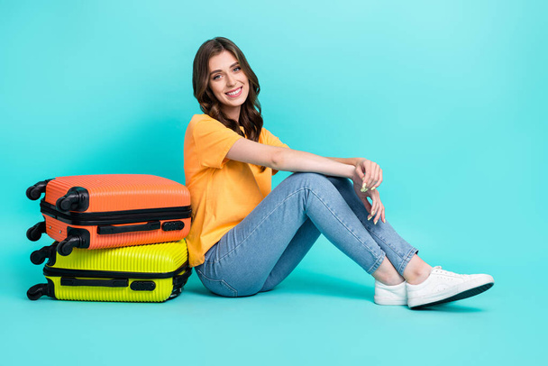 Full length photo of cute adorable girl dressed yellow t-shirt sitting floor packing luggage isolated teal color background. - 写真・画像