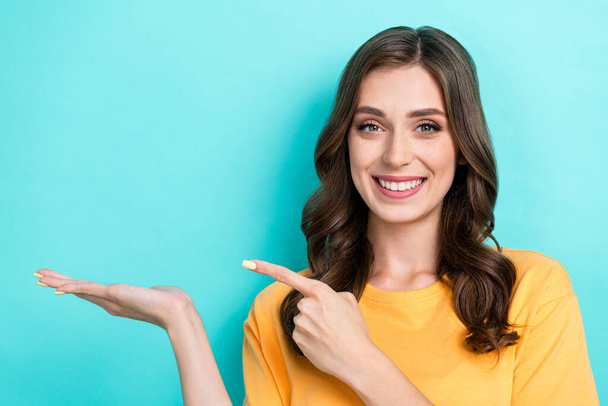 Portrait of lovely sweet good mood girl wear yellow t-shirt palm showing offer finger directing product isolated on teal color background. - Foto, Imagem