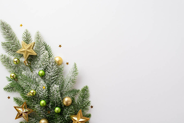 Nieuwjaarsconcept. Bovenaanzicht foto van dennentak met gouden en groene kerstballen gouden ster ornamenten en glanzende confetti op geïsoleerde witte achtergrond met lege ruimte - Foto, afbeelding