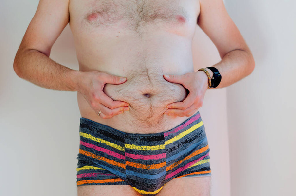 Mann in Unterwäsche mit dickem Bauch, übergewichtiger männlicher Körper isoliert auf weißem Hintergrund. Abnehmen. Konzept der Chirurgie, subkutane Fettabbau. Körper positiv - Foto, Bild