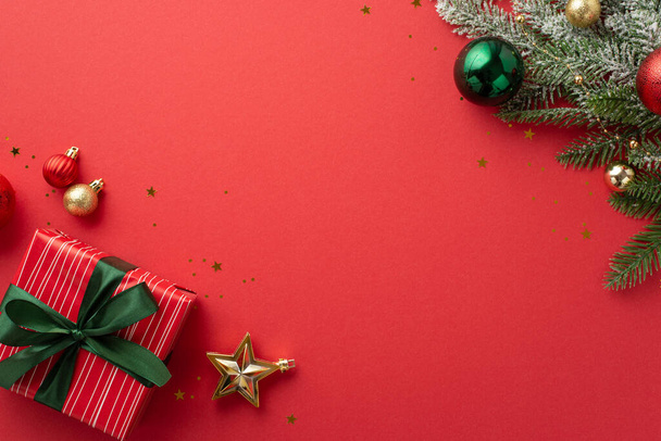 クリスマスのコンセプト。緑の金と赤の泡で飾られた松の枝のトップビューの写真コピースペースと隔離された赤の背景にリボン弓とコンフェッティと星の装飾大きなギフトボックス - 写真・画像